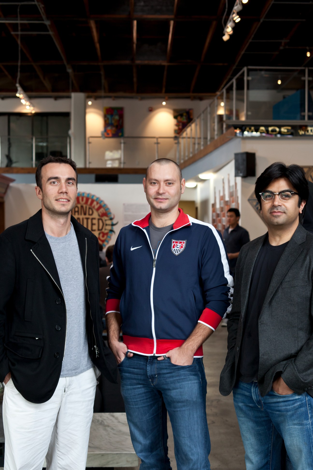 Three men standing in a modern office space with exposed ceiling and industrial design.