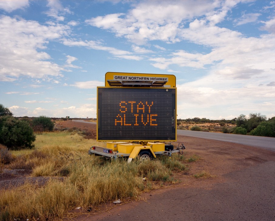 Digital road sign on Great Northern Highway displaying 'STAY ALIVE' safety message in outback landscape.