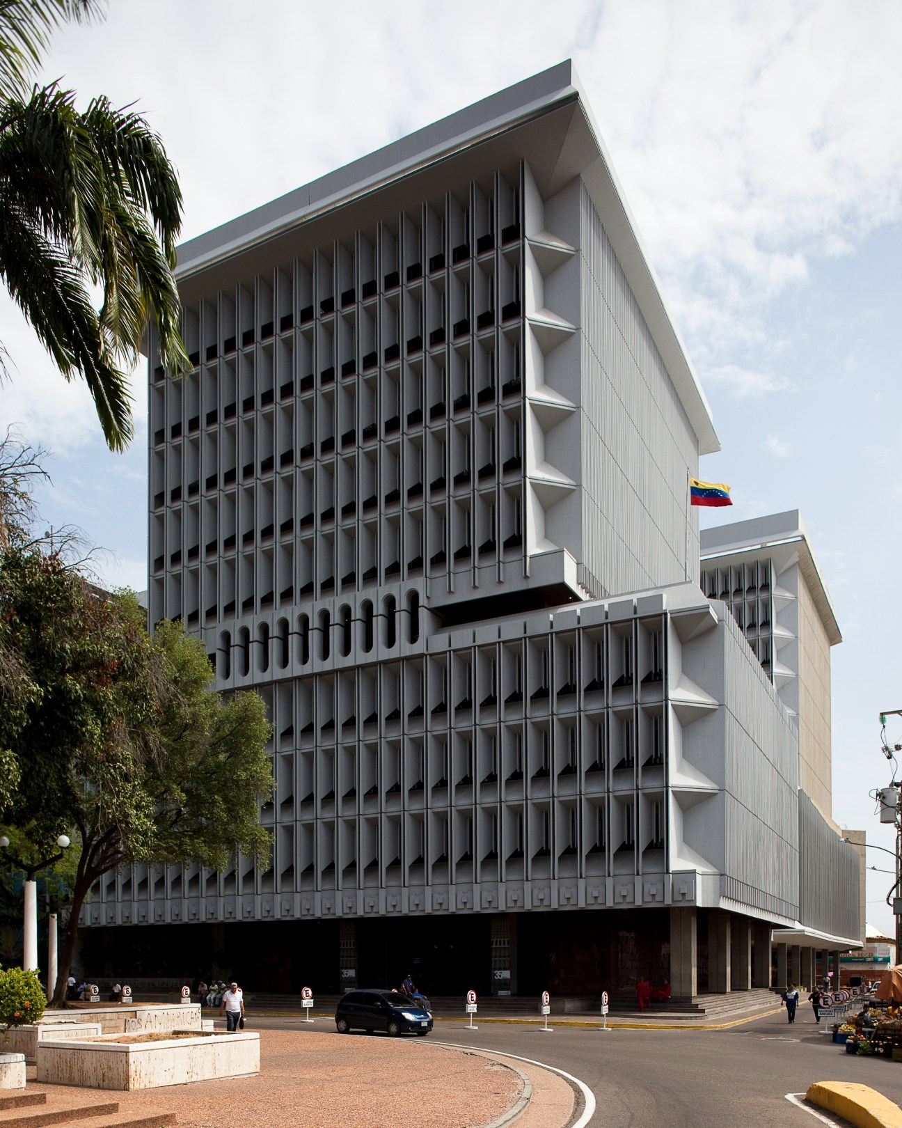 Modern white building with vertical ribbed facade and Venezuelan flag, housing the Maracaibo Central Bank branch.