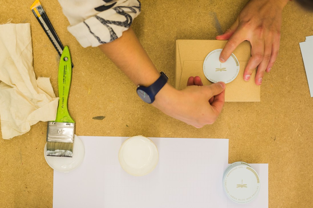 Hands carefully applying a label to a cardboard box containing printed notepads at Le Typographe.