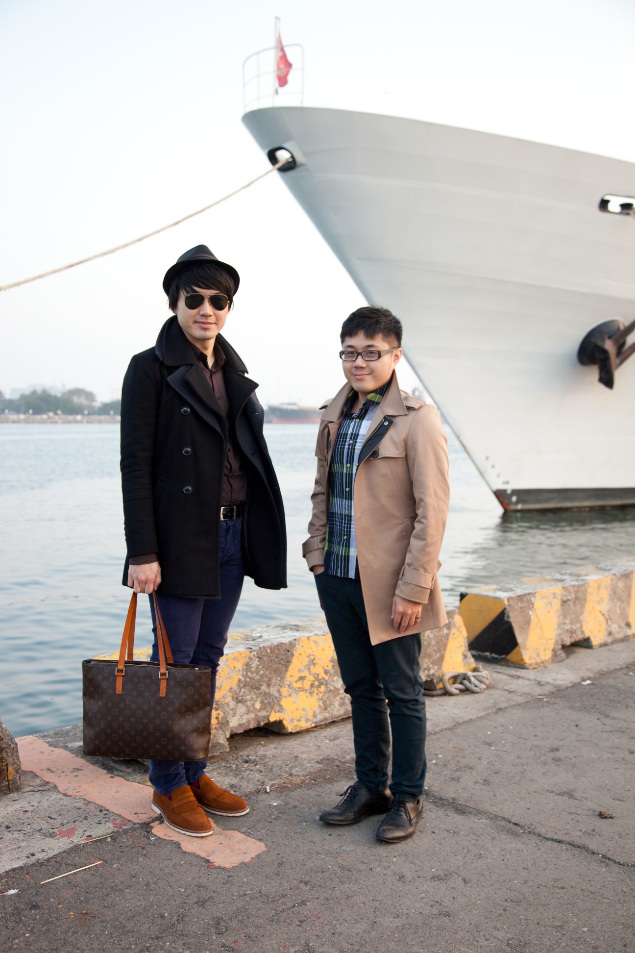 Two men stand on a harbor dock in front of a docked yacht in Kaohsiung.