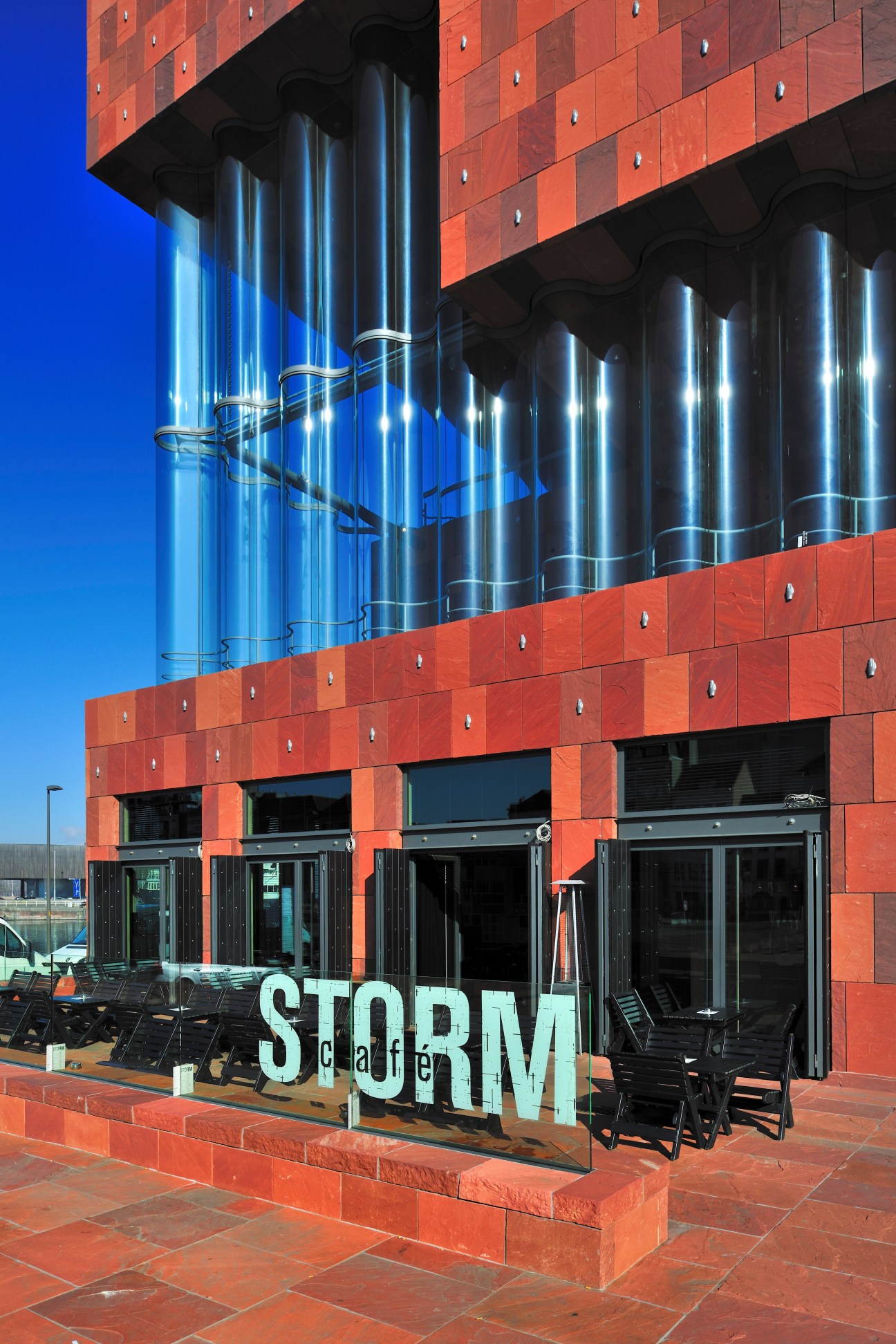 Café Storm exterior with red brick facade, glass doors, and blue steel columns under clear sky.