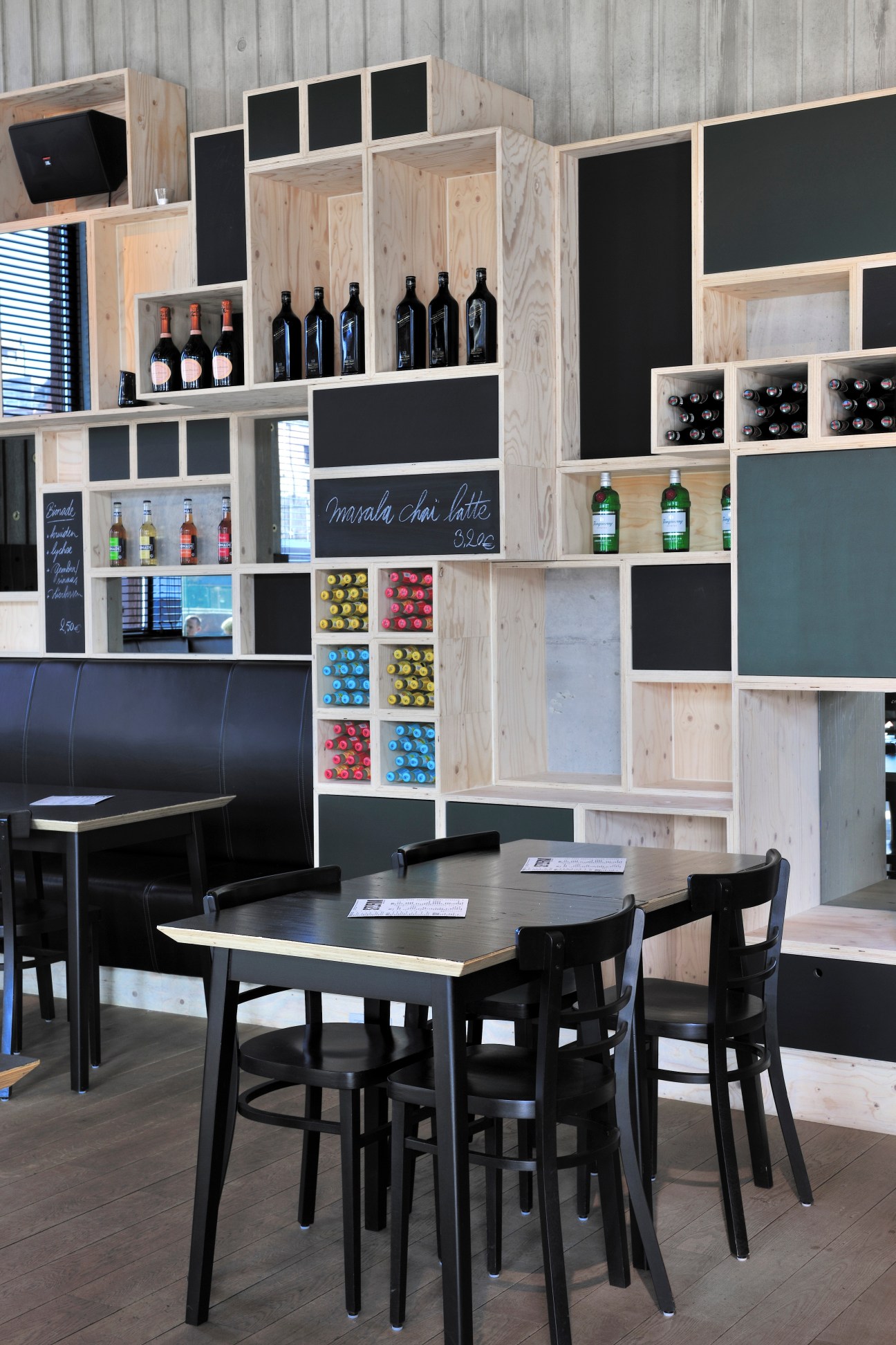 Interior of Café Storm with wooden shelving displaying wine bottles, a black dining table with chairs, and chalkboard menu.