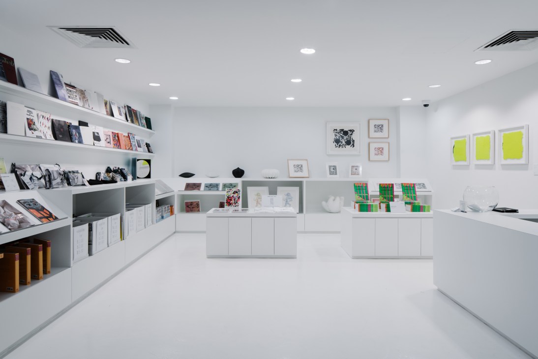 STPI gallery shop with white walls, shelving displaying art books and prints, framed artworks, and colorful paper samples.