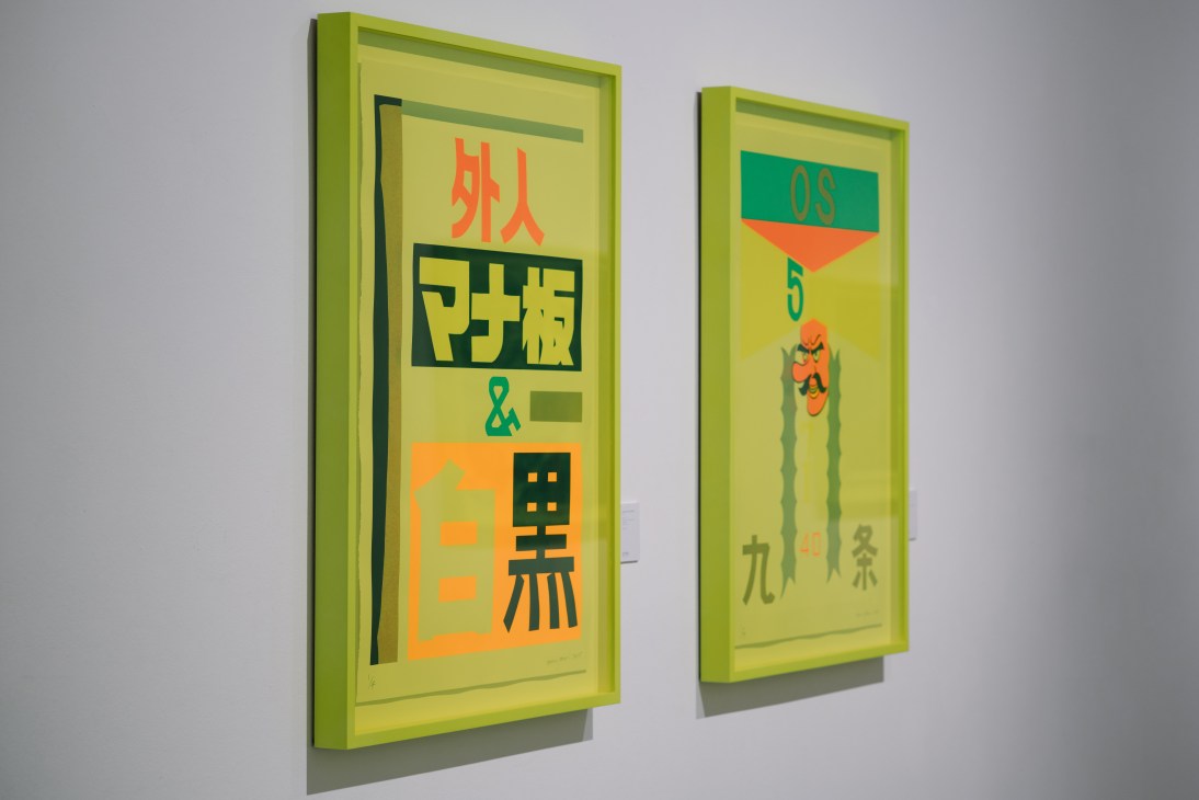 Two framed screenprints on bright yellow-green backgrounds featuring Asian characters and geometric shapes in orange and teal.