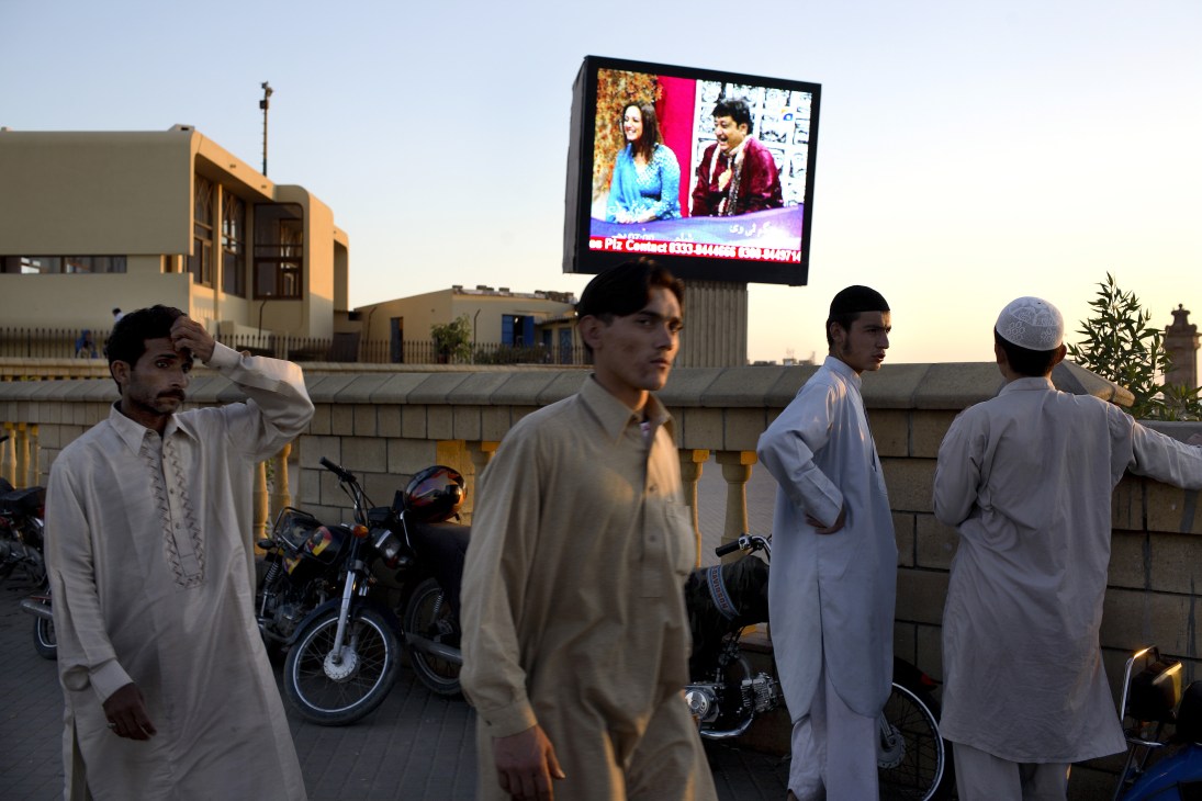 Pakistani men watch a television broadcast on a large outdoor screen in Karachi's Clifton seafront area at dusk.