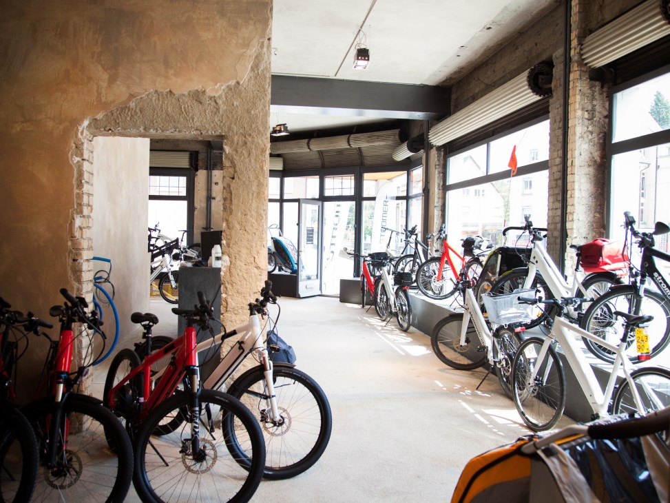Interior of a modern e-bike retail store with multiple bicycles in red, white and black displayed on the floor and against walls.