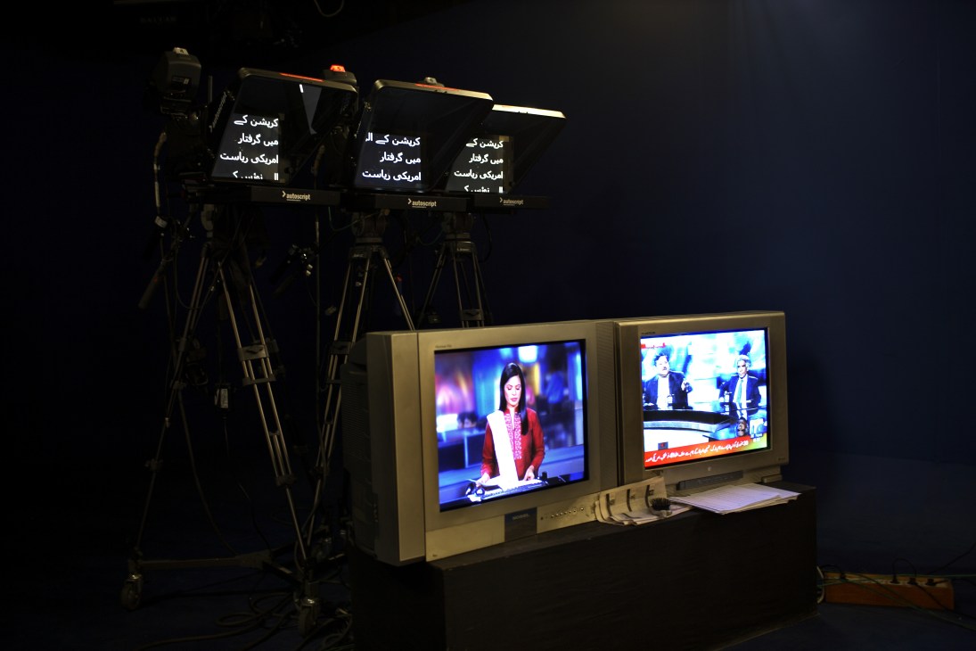 Television studio setup with autocue screens displaying Urdu text and monitoring equipment showing news presenters.