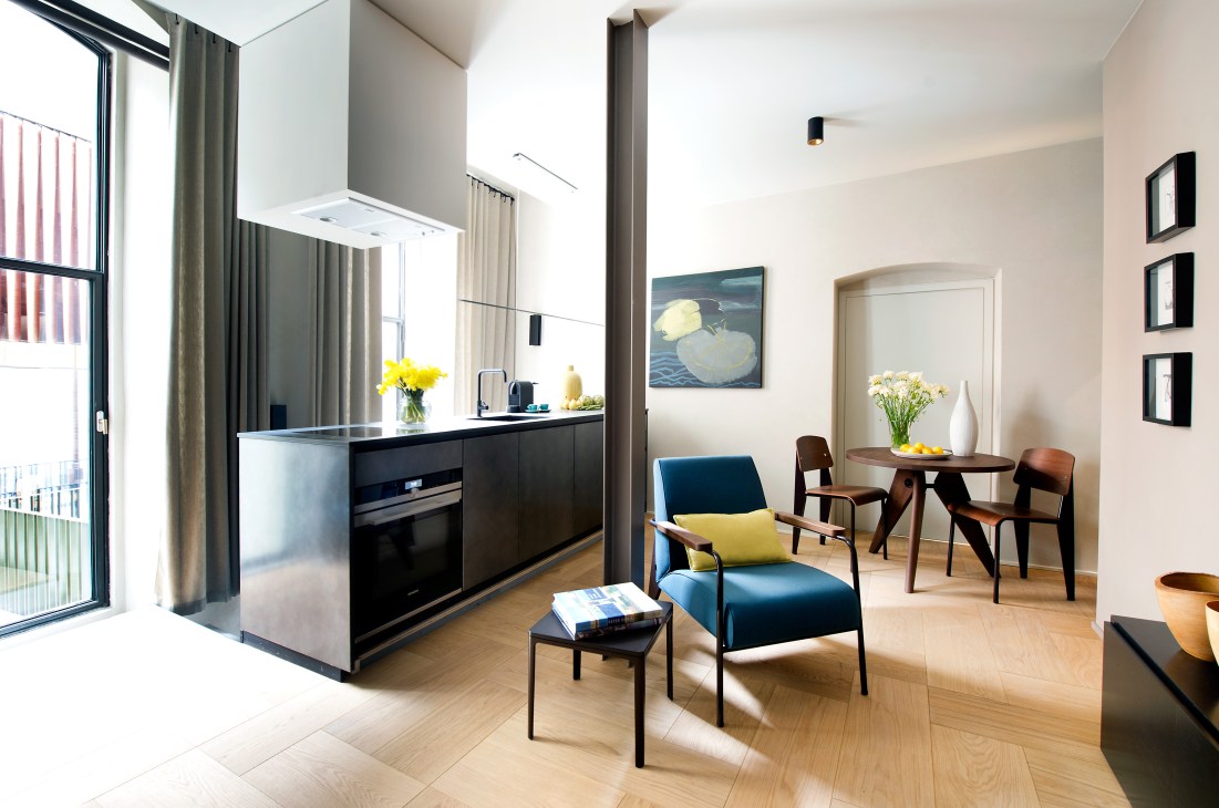 Modern apartment interior at Nest Geneva with open-plan kitchen, dining area and contemporary furnishings including Eames chairs.