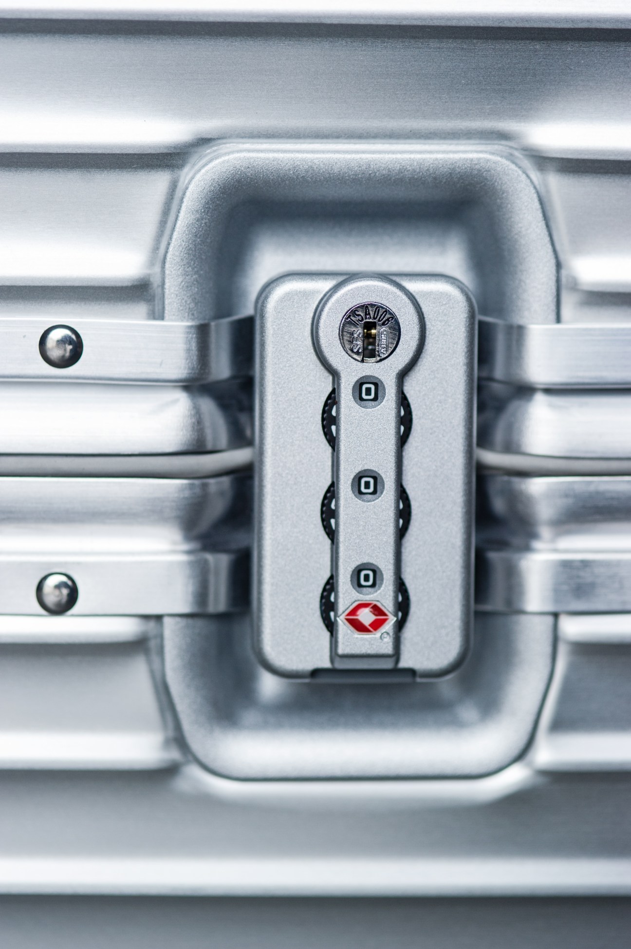 Close-up of a silver combination lock on a Rimowa aluminum suitcase with grooved ribs.