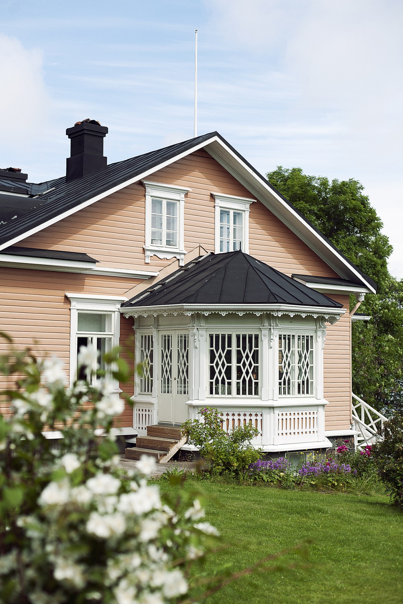 A traditional wooden villa with tan siding, white-trimmed windows, and a distinctive white gazebo pavilion with a black roof.