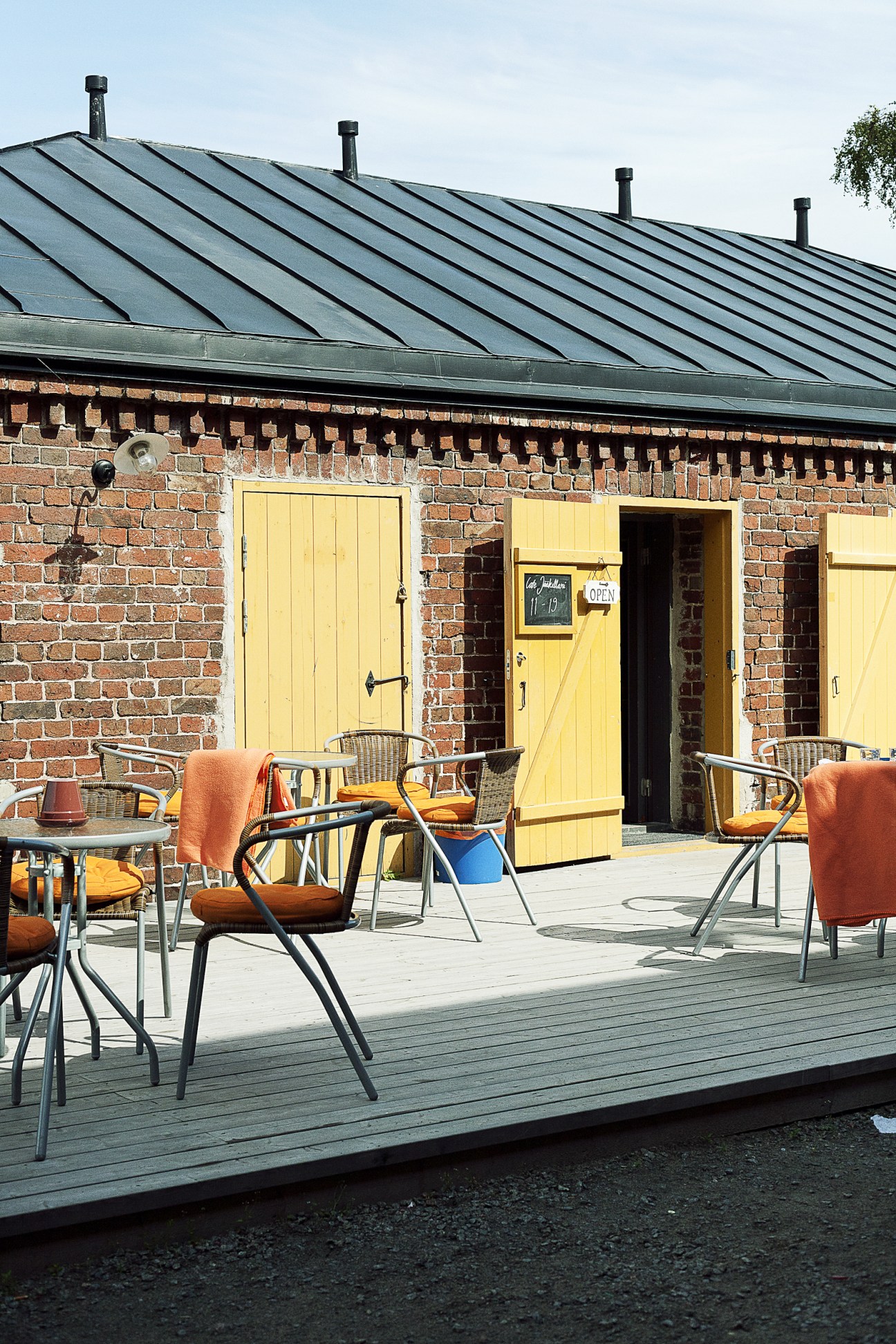 Café Icecellar's brick exterior with yellow doors and a metal roof, featuring an outdoor seating area with orange chairs.