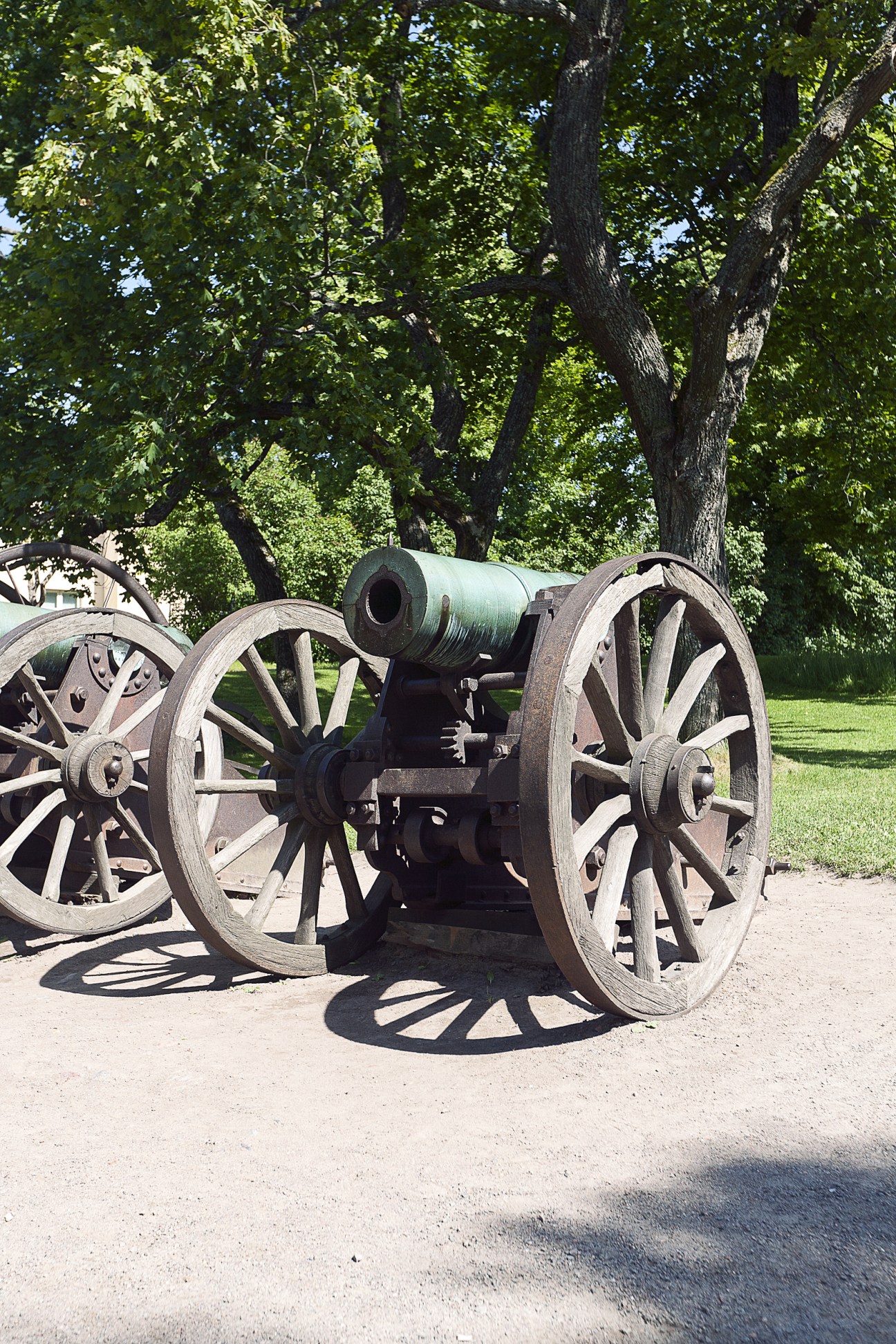 Historic cannons with wooden wheels displayed under trees on Suomenlinna fortress grounds.