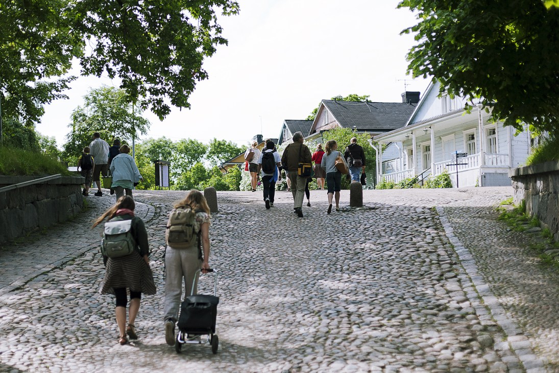 Tourists and visitors walking on a cobblestone street lined with historic white wooden buildings in Suomenlinna.