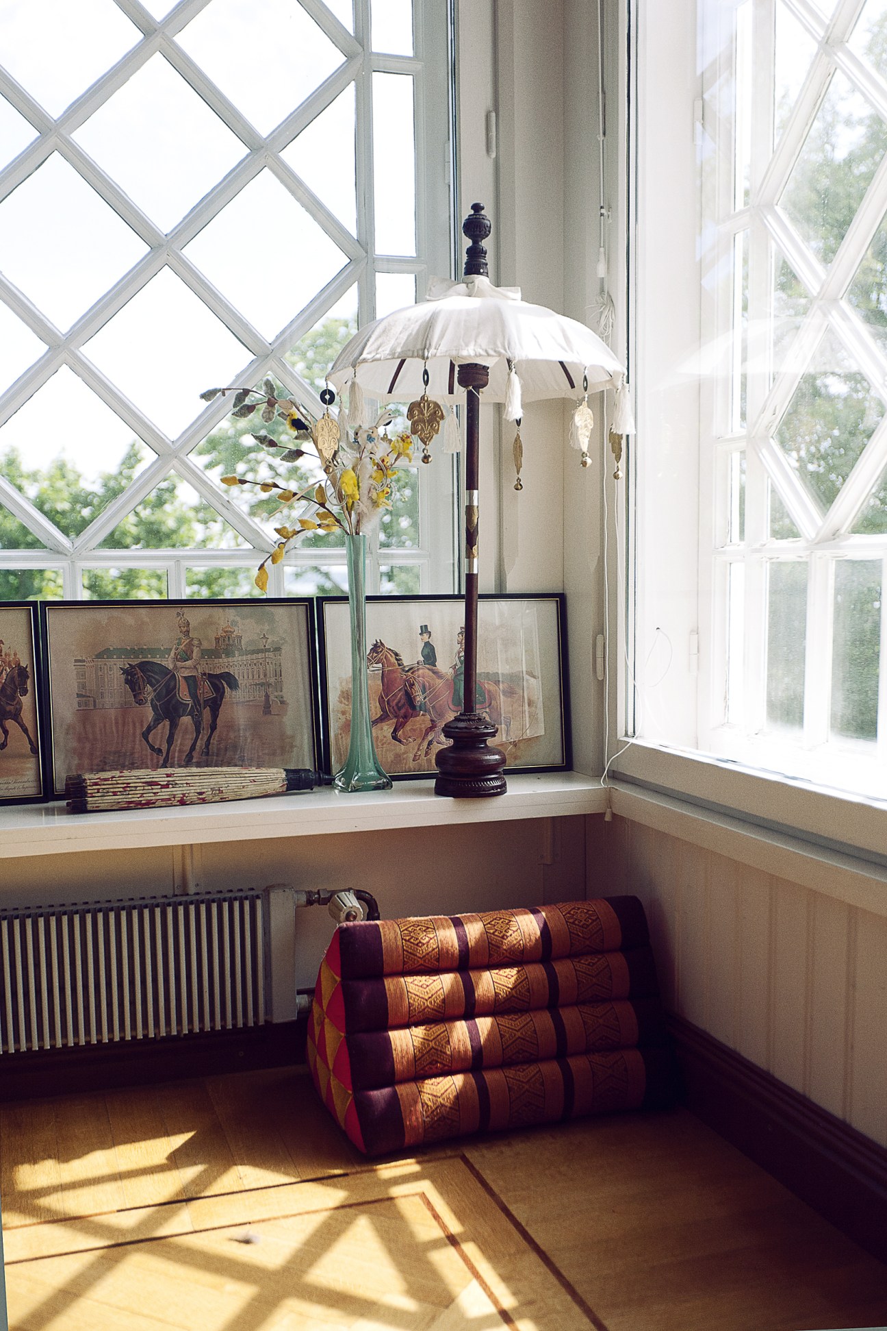 A bright conservatory with latticed windows displaying vintage prints, decorative umbrella, and leather-bound books.