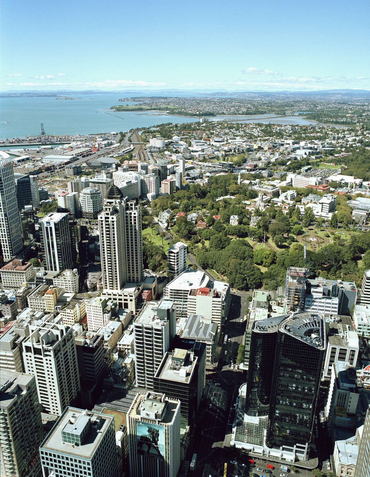 Aerial view of Auckland's downtown skyline with harbours, residential areas and green spaces visible in the distance.