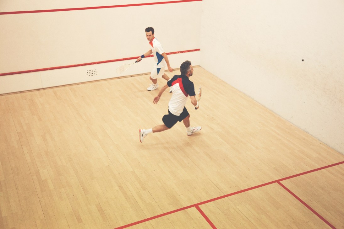 Two men playing squash on an indoor court with red lines, holding Wilson racquets.