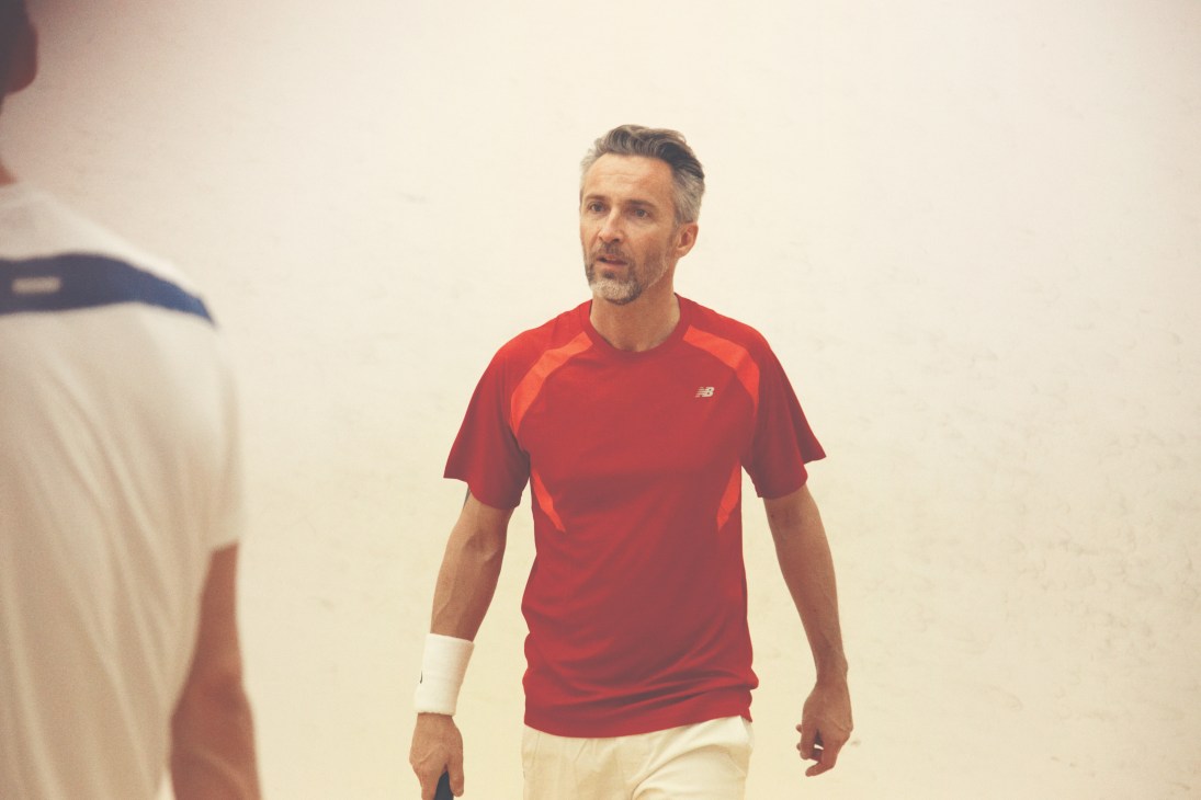 Man wearing red New Balance t-shirt and white shorts on a tennis court