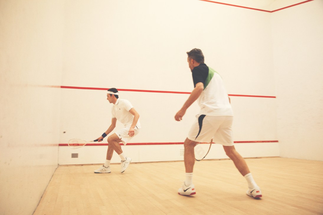 Two men playing squash on an indoor court with red lines and wooden floor.