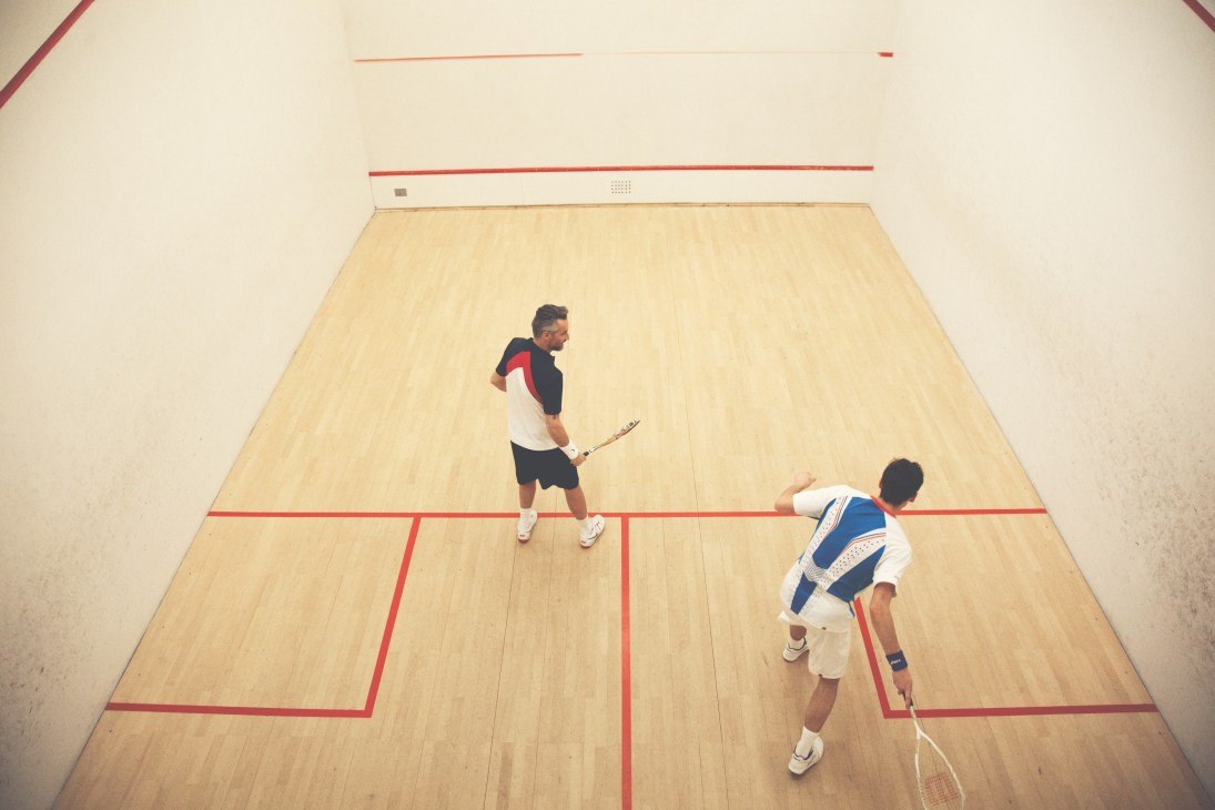 Two men playing squash on an indoor court with red lines on a wooden floor.