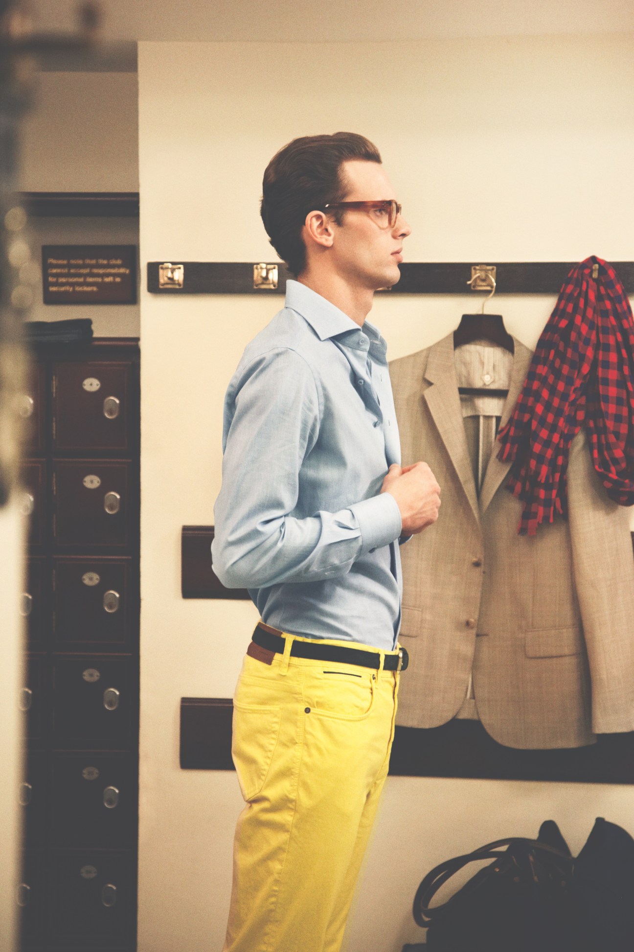 Man wearing Oliver Peoples glasses, Ermenegildo Zegna shirt, and Incotex yellow trousers in a clubhouse interior.