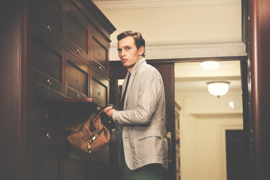 Man in light blazer and brown bag standing in wood-paneled clubhouse hallway