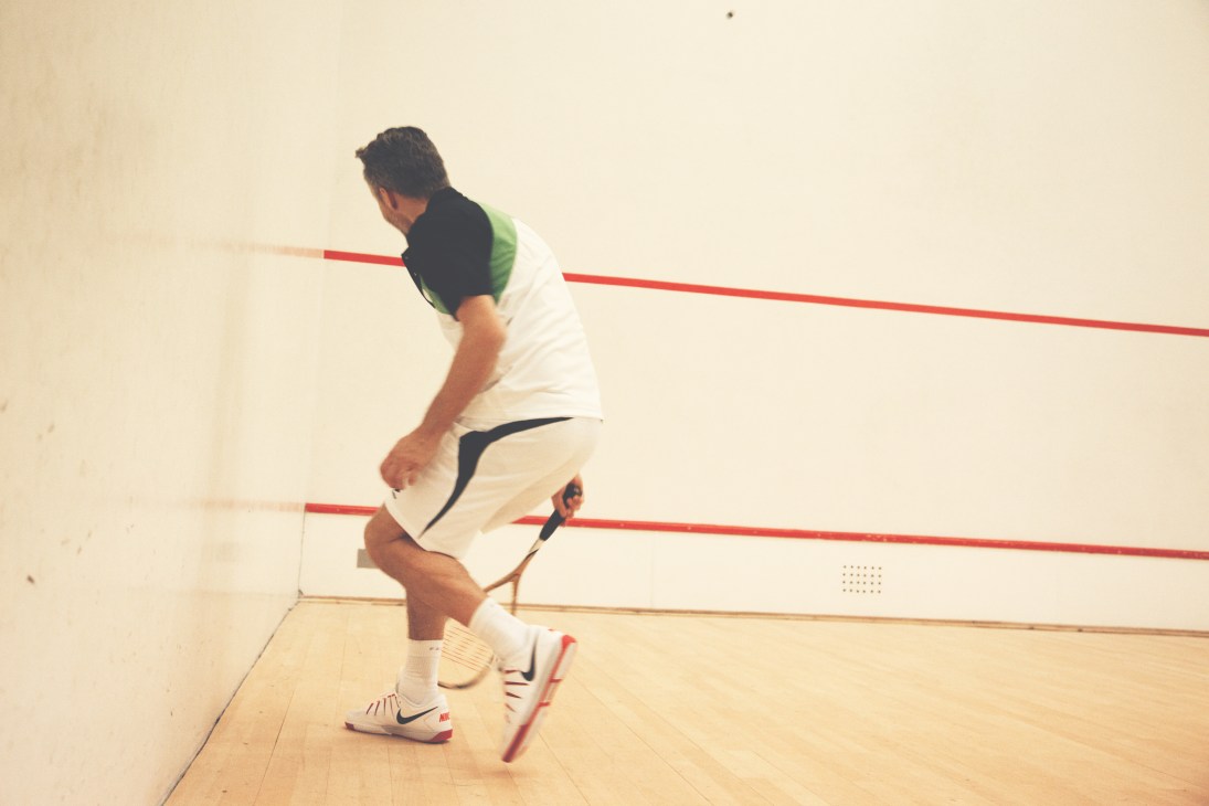 Player in white shorts and Nike shoes playing squash on indoor court with red lines.