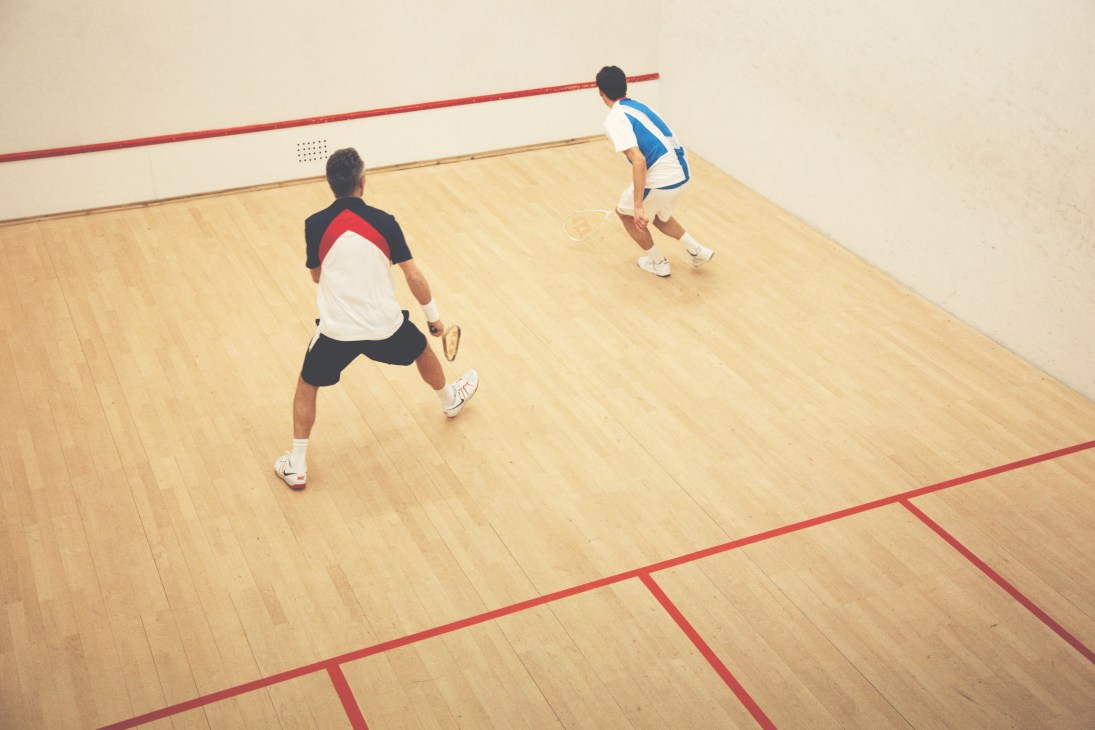 Two players compete on a squash court, one in a navy and white shirt, the other in blue and white, both holding racquets.