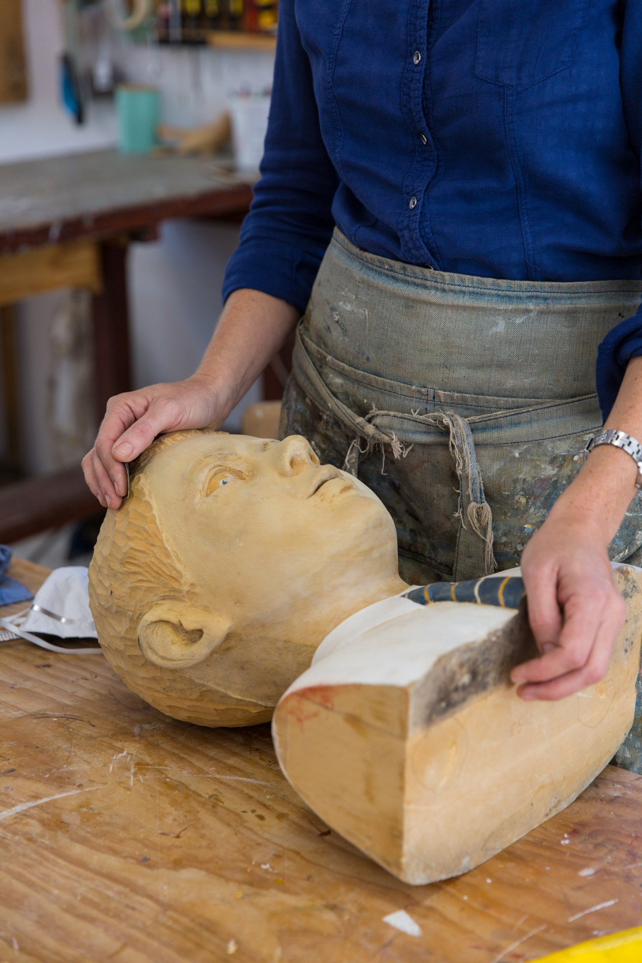 Artist's hands working on a wooden carved sculptural head in a studio.
