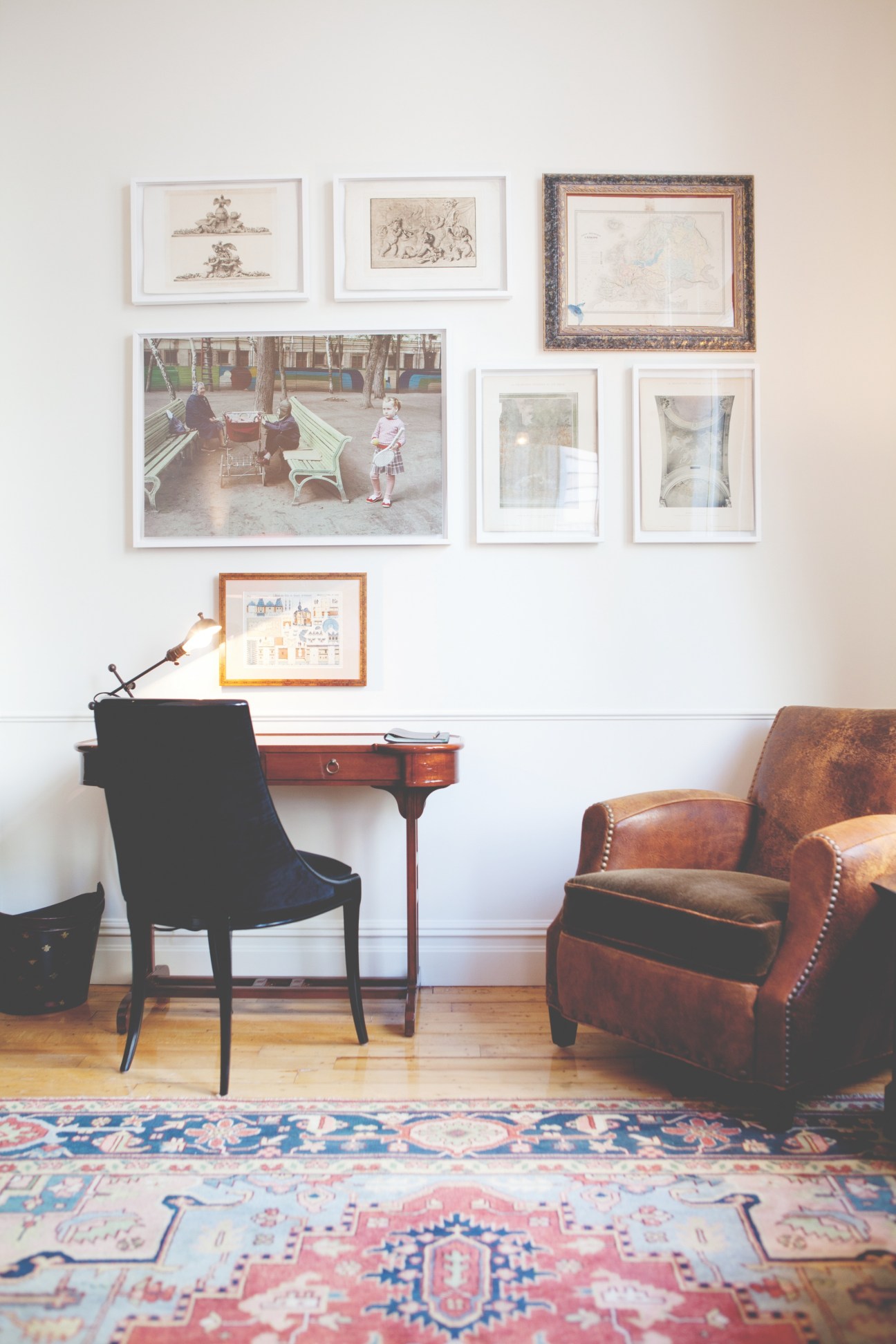 Corner suite sitting room with mismatched framed artworks, leather armchair, desk with task lamp, and patterned rug.