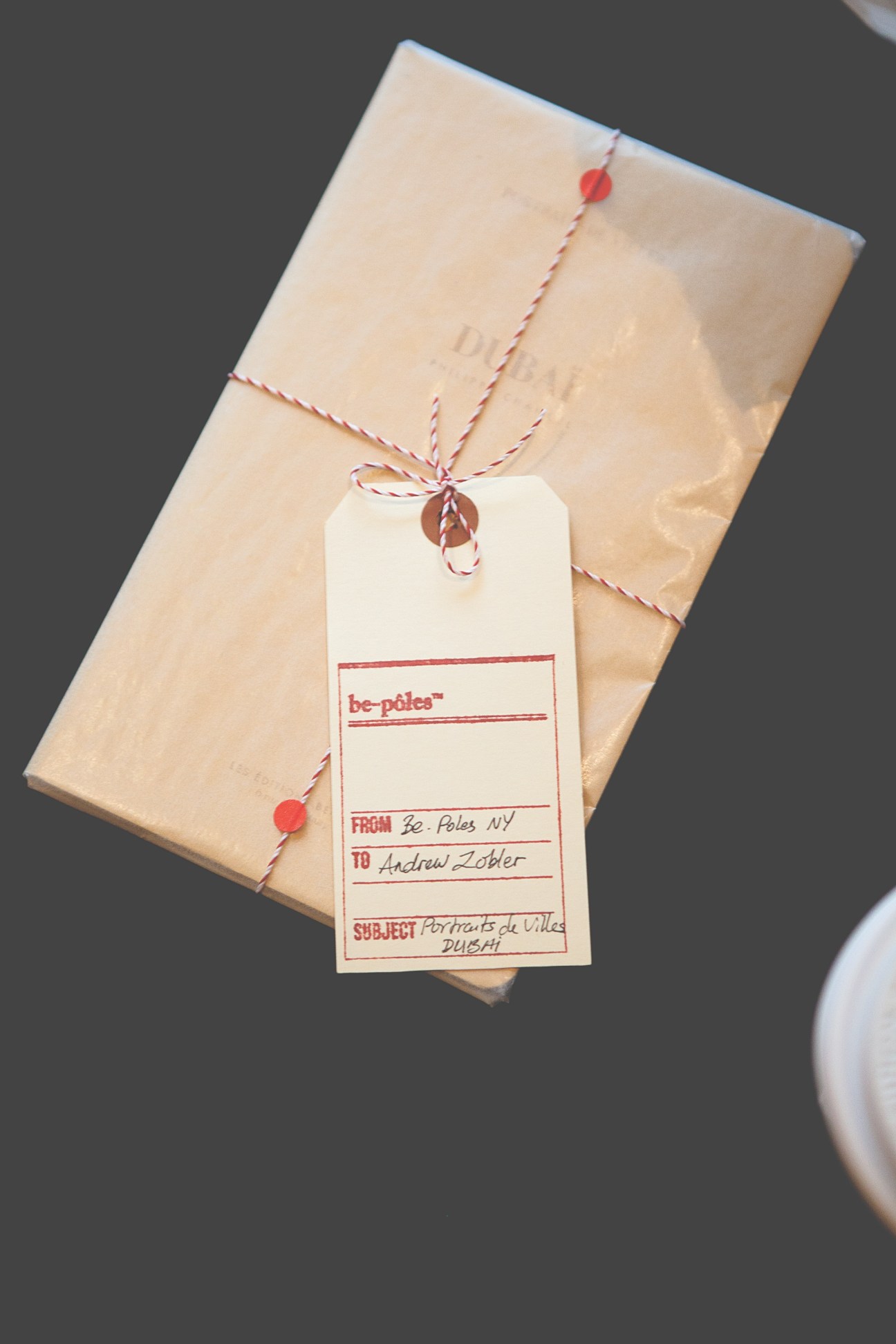 Be-pôles photo book wrapped in kraft paper with red and white twine and a shipping tag labeled 'be-pôles'.
