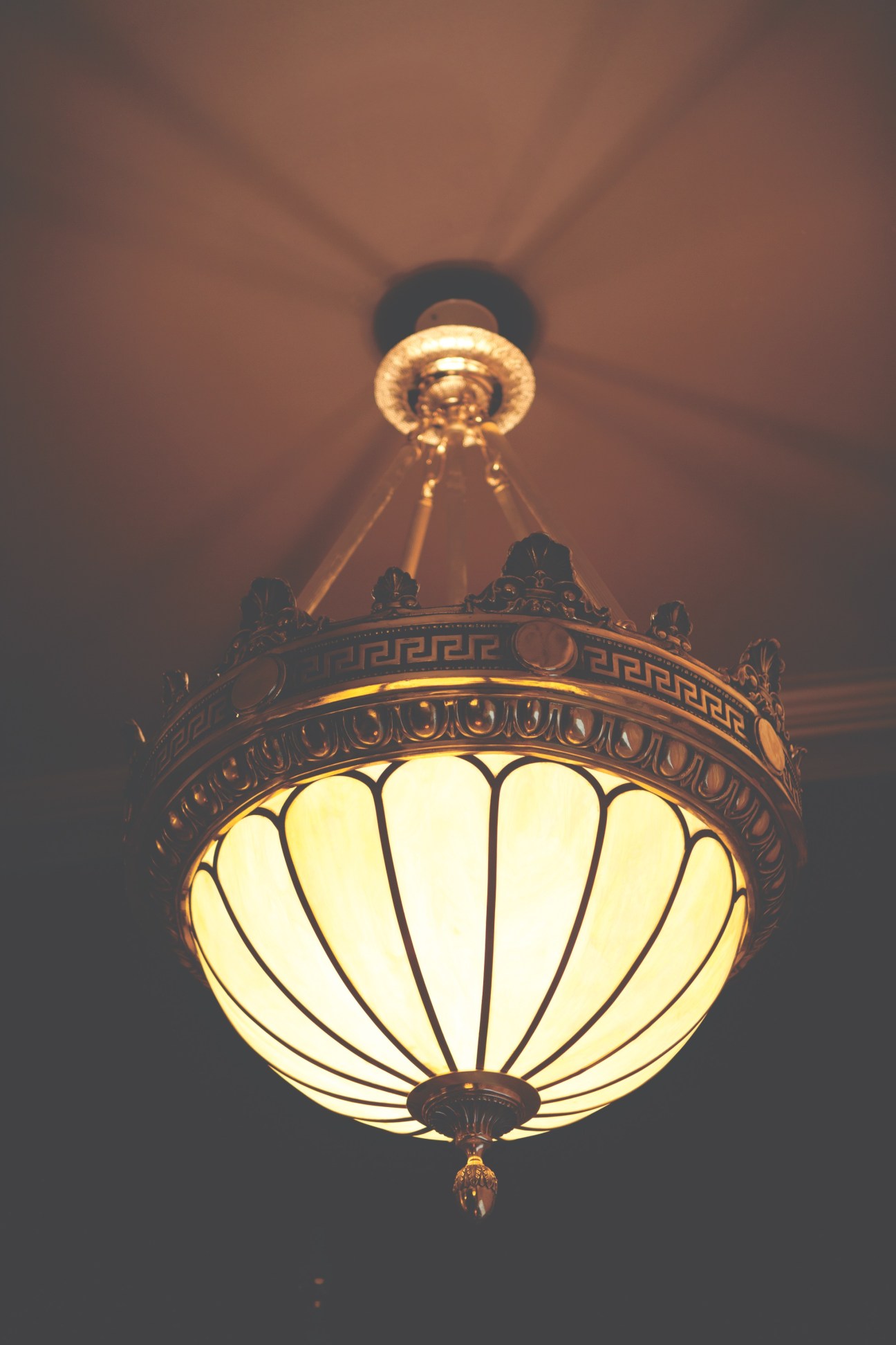 Ornate pendant light fixture with illuminated cream-colored dome and decorative bronze metalwork casting shadows on ceiling.