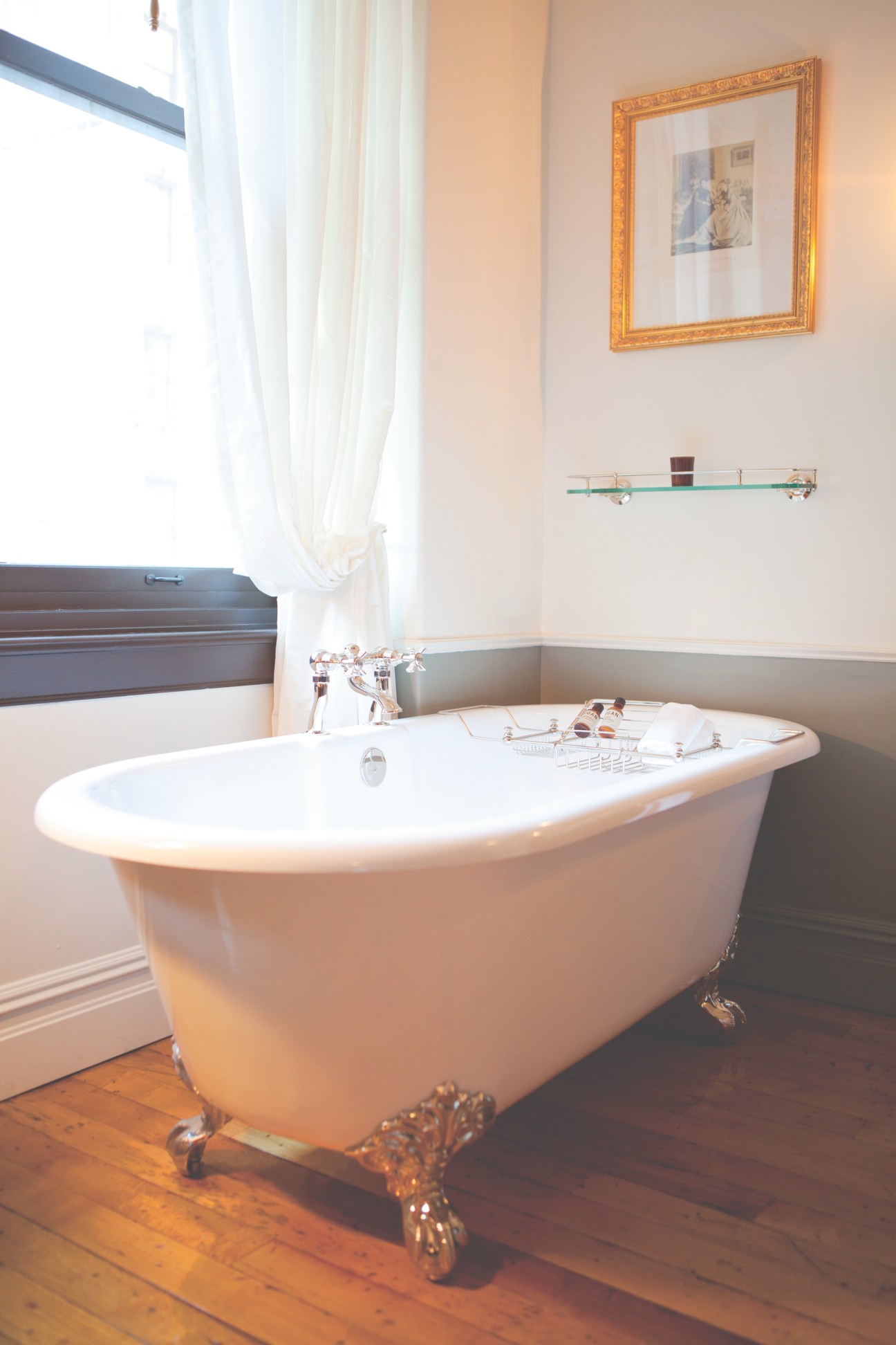 White freestanding bathtub with ornate claw feet in a light-filled hotel bathroom with a large window.