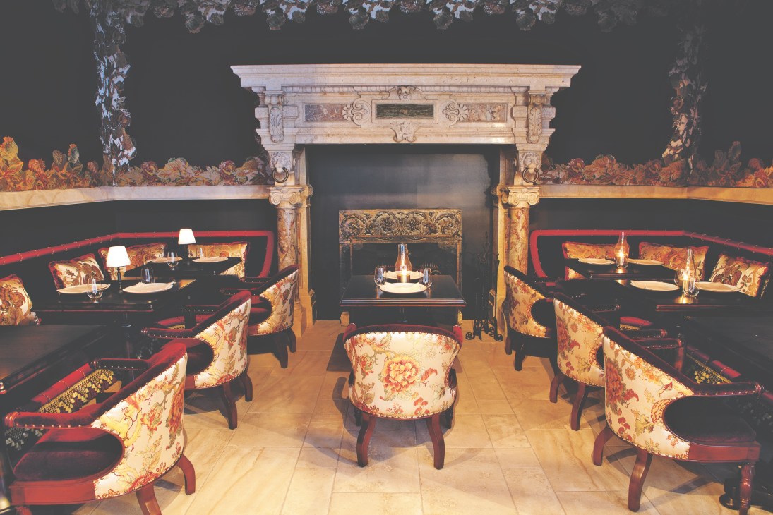 NoMad Hotel dining room with ornate fireplace, floral upholstered chairs and red trim.