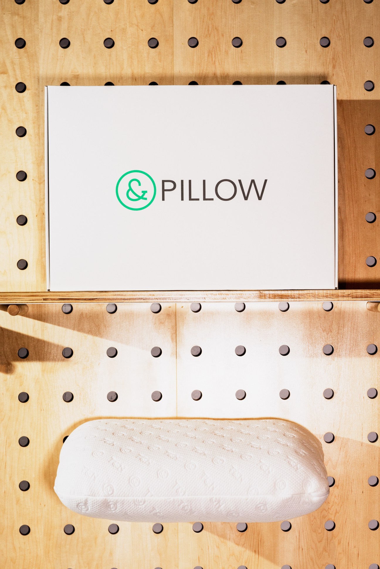 T&N branded pillow with logo displayed on white packaging against wooden pegboard.