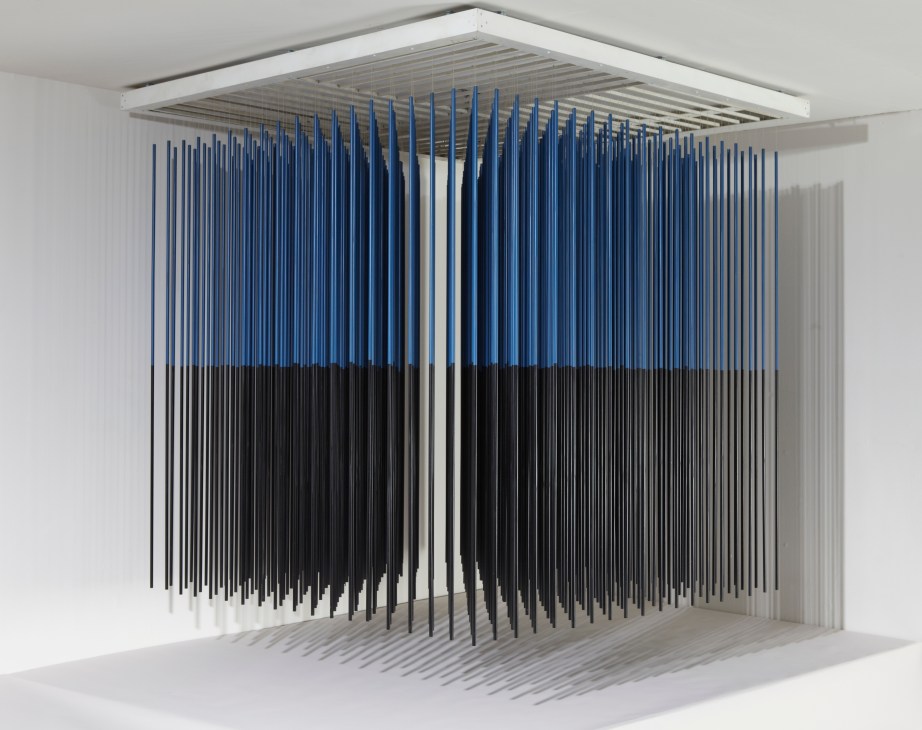 Abstract kinetic installation with blue and black vertical rods suspended from white ceiling structure.