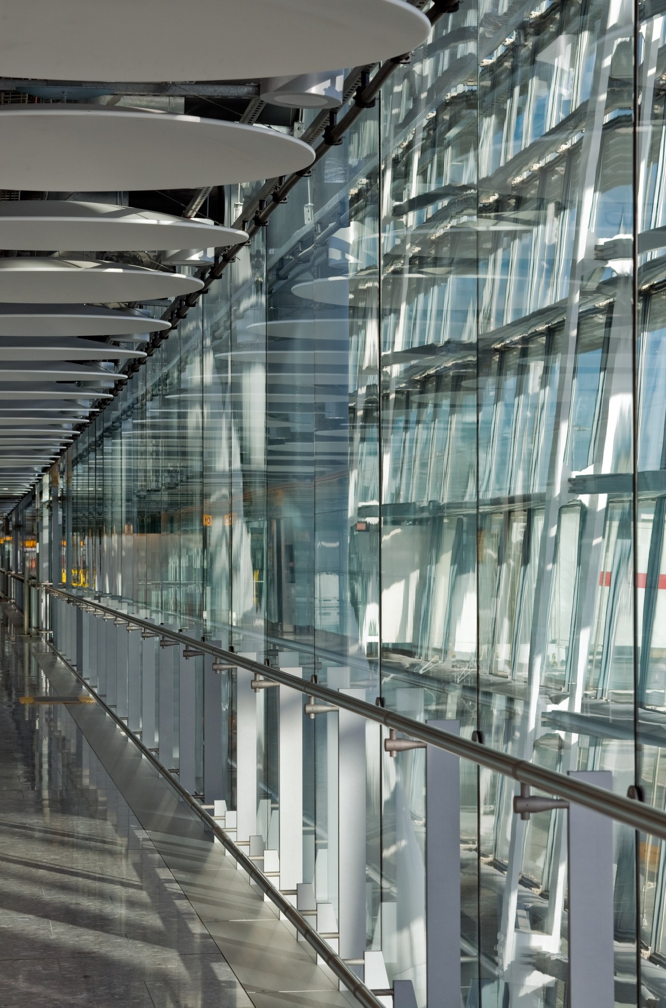 Heathrow Terminal 5 corridor with glass walls, white ceiling panels and metal railings.