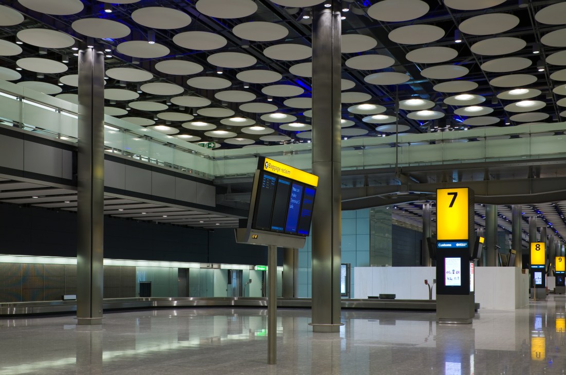 Modern airport terminal interior with circular ceiling lights, support columns, and yellow gate signs.