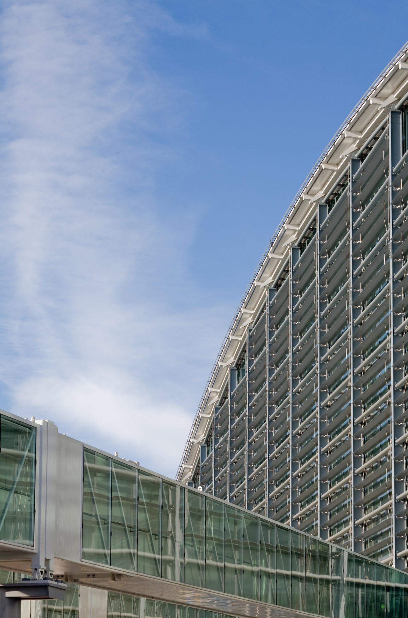 Exterior view of Heathrow Terminal 5 showing distinctive curved glass and metal facade against blue sky.