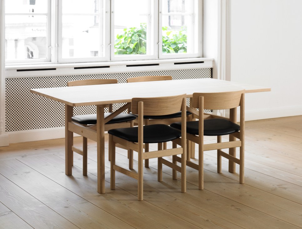 Wooden dining table with white top and four matching chairs with black seats in a minimalist interior.