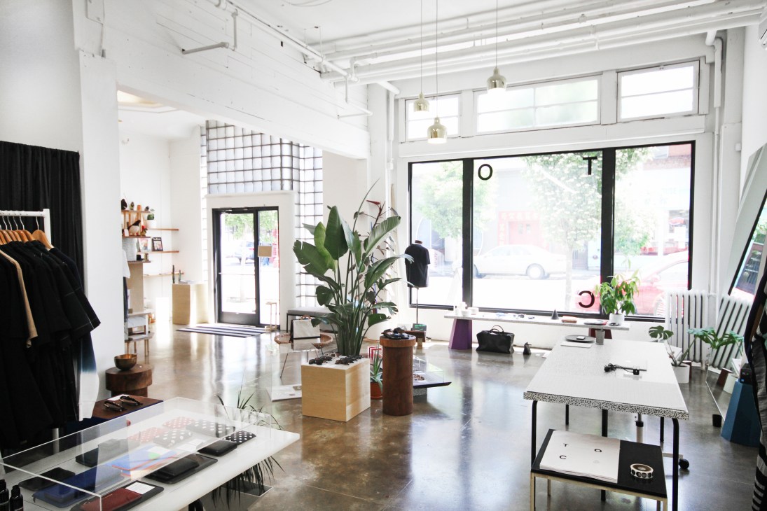 Interior of Table of Contents shop in Portland showing white walls, polished concrete floors, hanging brass pendant lights, and displays of black clothing and home goods.