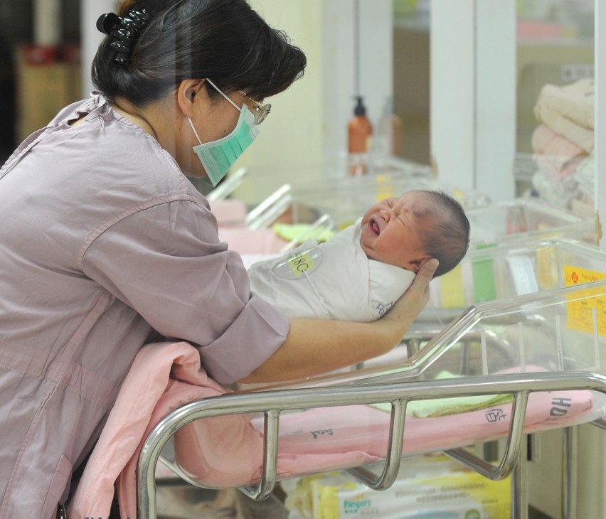 Healthcare worker holding a newborn infant in a hospital nursery setting.