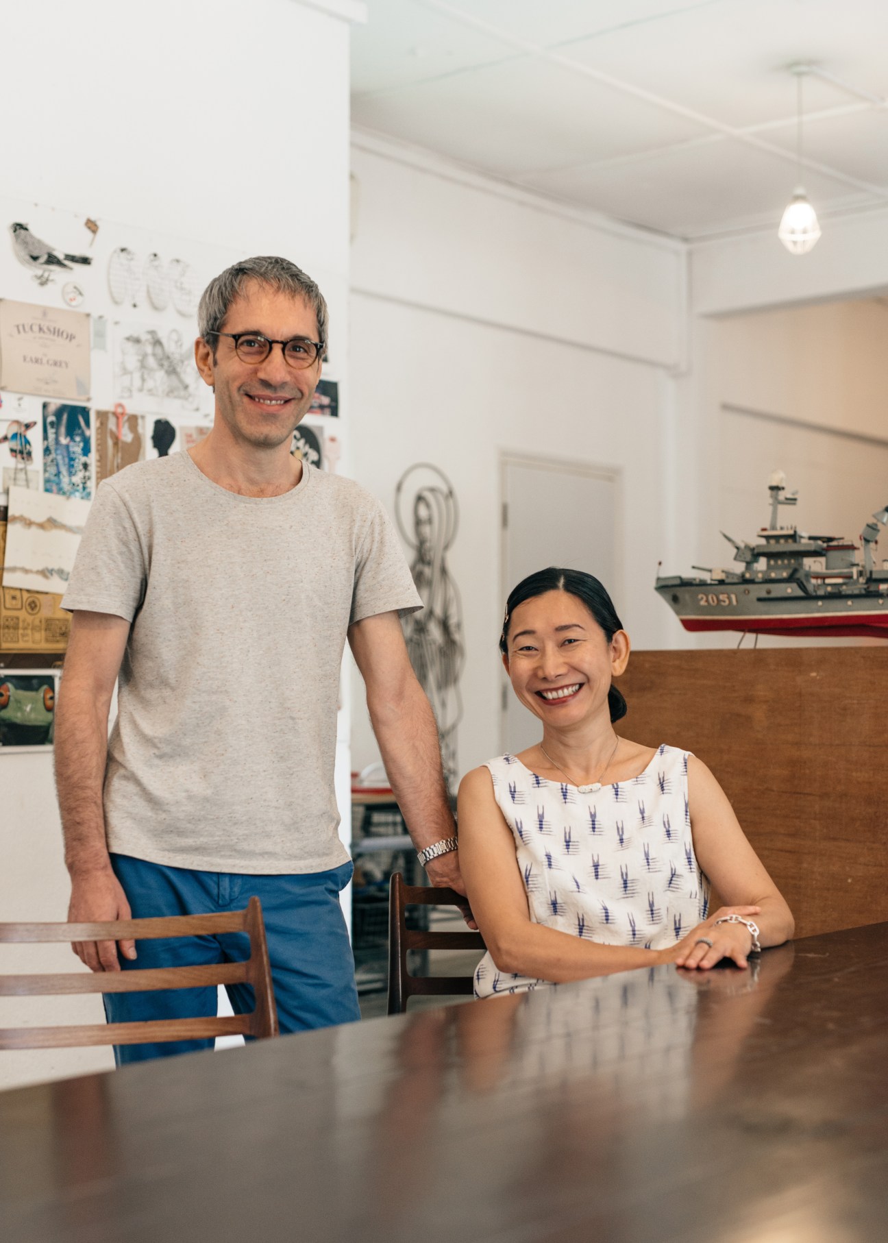 Two people standing and sitting at a table in an office with design materials on walls