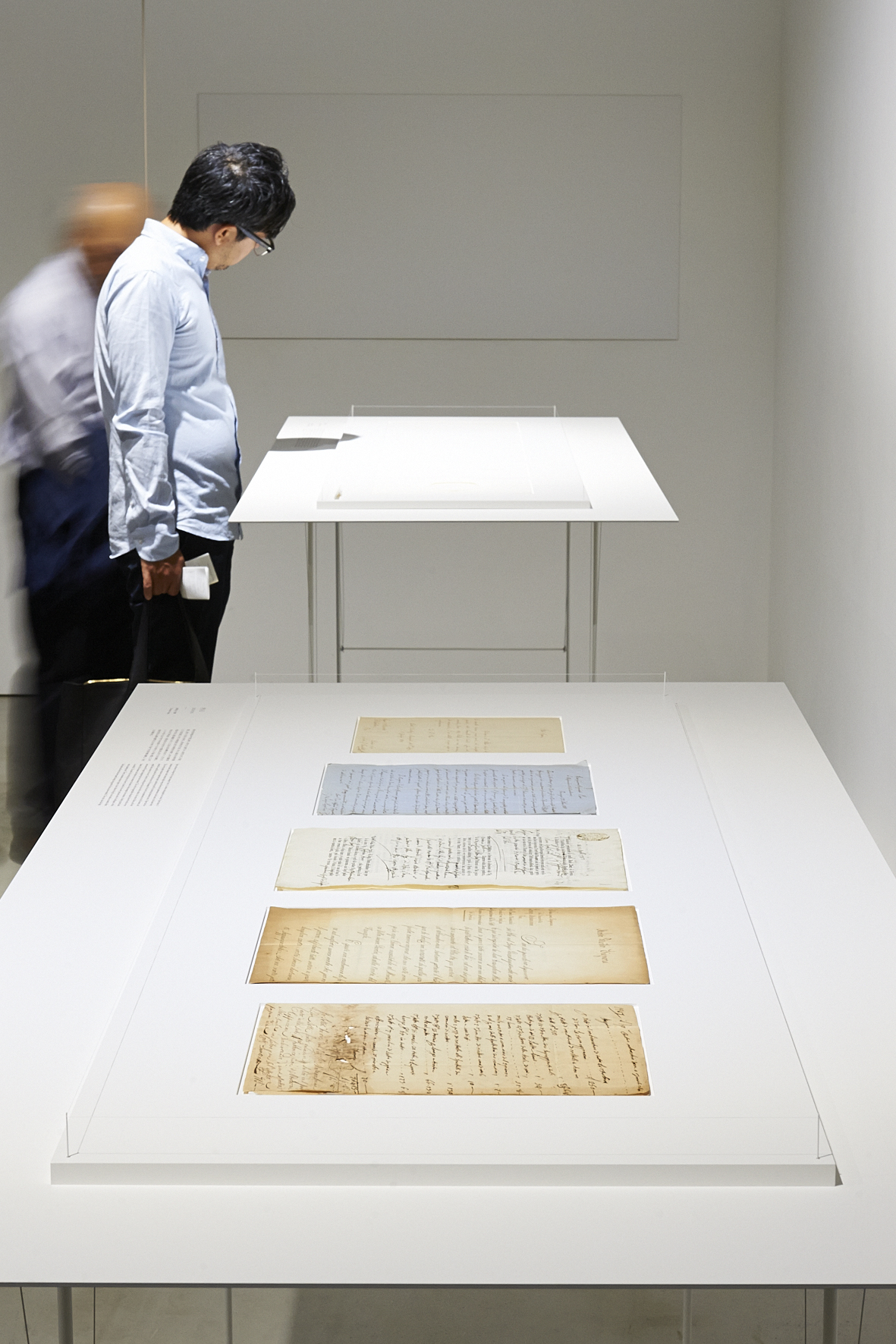 Visitor viewing calligraphy examples displayed on white tables at the Takeo Paper Show exhibition.