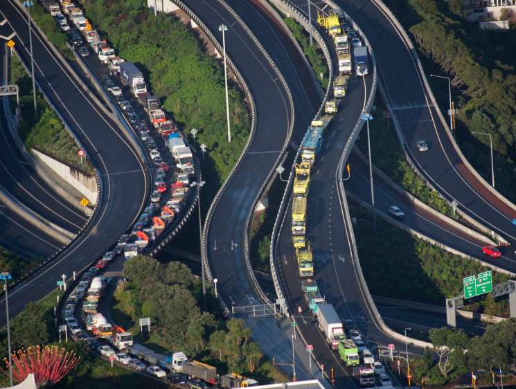 Aerial view of congested multi-lane motorway interchange with heavy traffic and surrounding vegetation.