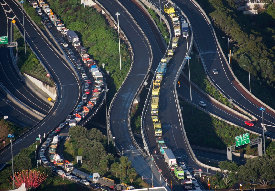 Aerial view of congested multi-lane motorway interchange with heavy traffic and surrounding vegetation.