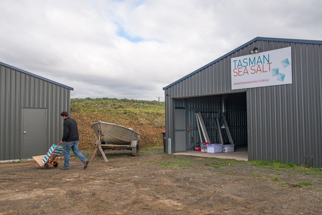 Man pushing hand truck loaded with supplies outside Tasman Sea Salt farm sheds in Tasmania.