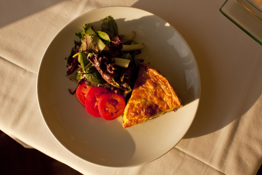 Quiche Lorraine served on a white plate with tomato slices, asparagus, and mixed greens.
