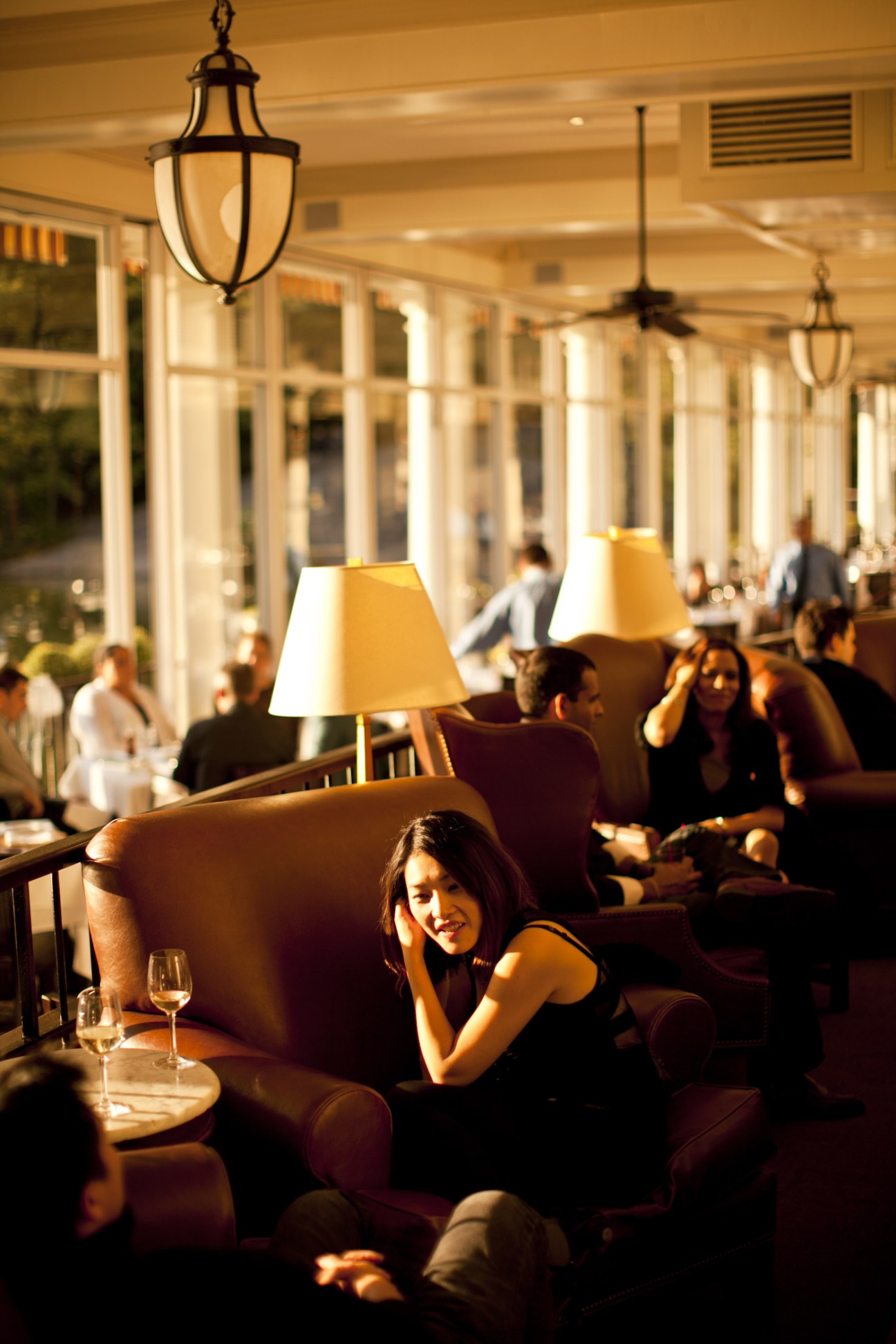 Woman in black dress at Central Park Boathouse bar with pendant lamps and large windows behind her.