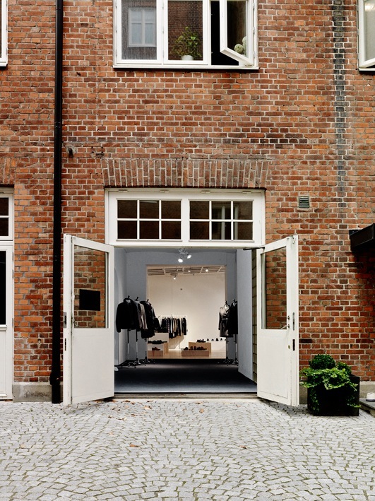 Très Bien storefront in Malmö with red brick facade and white double doors displaying clothing on mannequins.